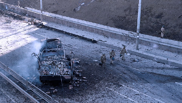 Tentara Ukraina berjalan melewati puing-puing dari truk militer yang terbakar di sebuah jalan di Kyiv, Ukraina pada 26 Februari 2022. (FOTO: BBC/AP Photo)