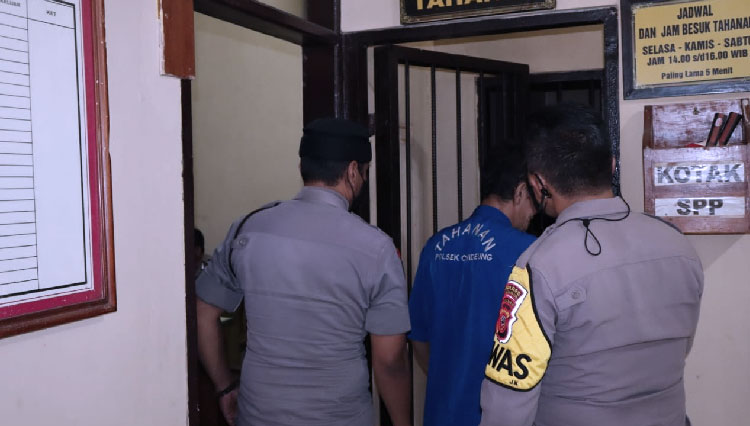Pria inisial IR (49) warga Kabupaten Garut yang mengaku dukun dan bisa menggandakan uang saat digiring oleh anggota Polsek Cihideung ke ruang tahanan. (Foto: Dok. Humas Polres Tasikmalaya Kota)