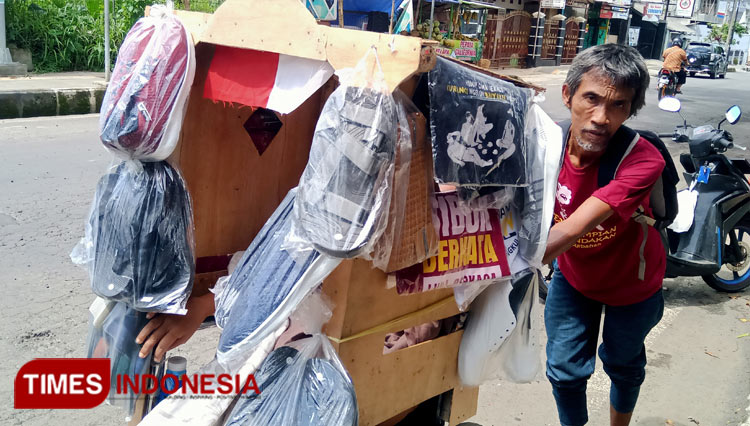 Wanto nampak sedang mendorong kursi roda yang diduduki istrinya sekaligus menjadi lapak jualan barang dagangannya (foto: Susi/TIMES Indonesia)