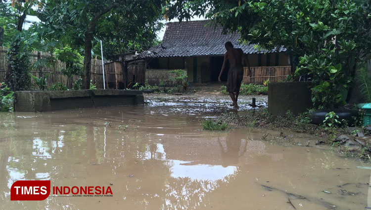 Warga membersihkan halaman rumah pasca diterjang banjir. (FOTO: Miftakul/TIMES INDONESIA)