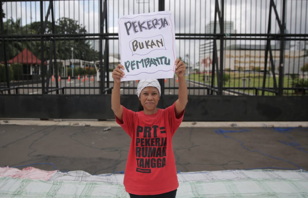 Salah satu peserta aksi yang tergabung dalam Koalisi Sipil Untuk UU Perlindungan PRT mengangkat poster di depan Gedung DPR.