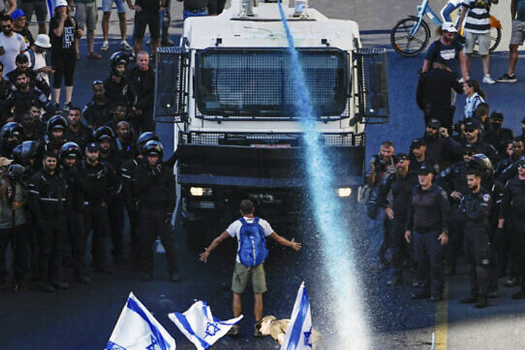 Seseorang berdiri di depan meriam air polisi Israel yang digunakan untuk membubarkan demonstran yang memblokir jalan selama protes terhadap rencana pemerintah merombak sistem peradilan. (FOTO : Times of Israel/AP)