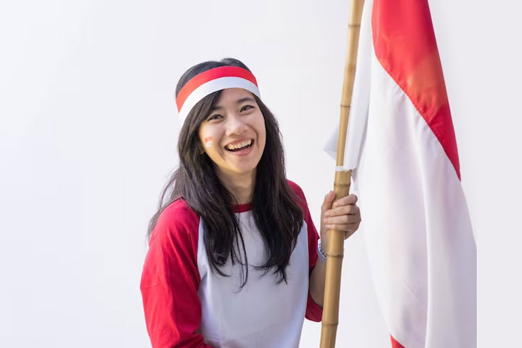 Gadis cantik memegang bendera Indonesia yang dipasang di sebilah bambu sambil memakai baju dan aksesoris serba merah putih. (Foto: Odua/Freepik)
