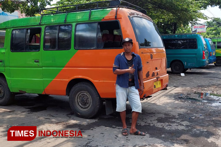 Yusuf (sopir angkutan) tengah berdiri lesu di mobil Bisonnya.(Foto: Rizky Putra Dinasti/TIMES Indonesia)