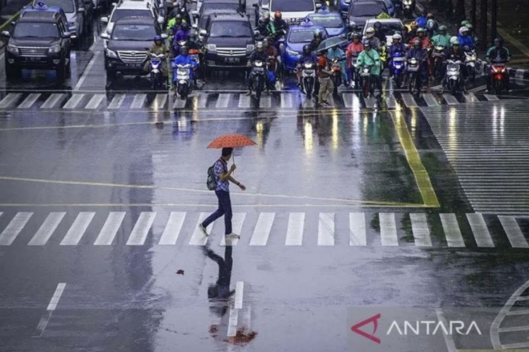 Seorang pekerja menggunakan payung untuk menghindari hujan saat menyeberang jalan di kawasan Jalan MH Thamrin, Jakarta. (ANTARA/Aprillio Akbar/hp/aa)