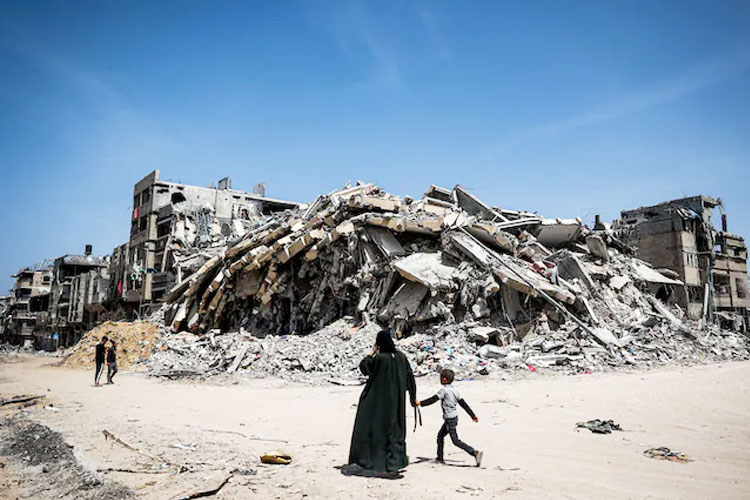 Seorang wanita dan anak-anak berjalan melewati bangunan yang hancur pada hari Senin di Khan Younis, Jalur Gaza. (FOTO: The Washington Post/AFP/Getty Images)