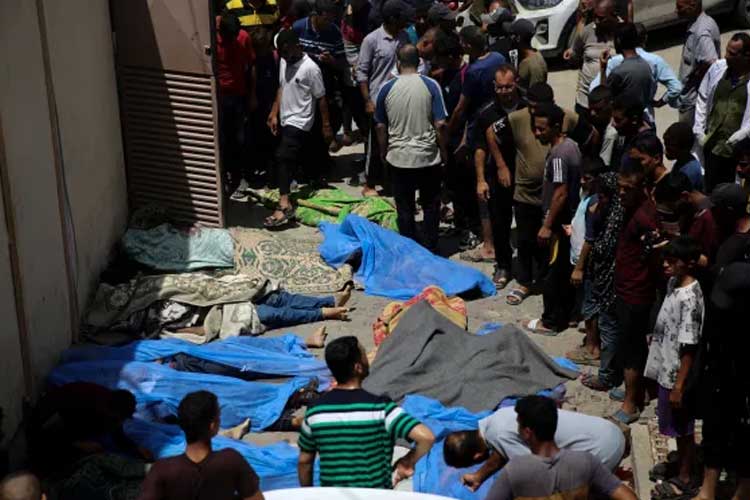 Warga Palestina berdiri di samping kerabat mereka yang meninggal dunia dalam pemboman Israel di Jalur Gaza di Rumah Sakit al-Aqsa di Deir el-Balah pada hari Sabtu. (FOTO: Al Jazeera/AP Photo)