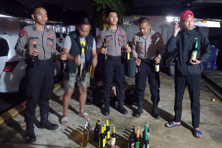 Sejumlah personel Polres Tasikmalaya Kota memperlihatkan beberapa botol miras hasil sitaan, Rabu (12/6/2024) dinihari. (FOTO: Dok. Polres Tasikmalaya)