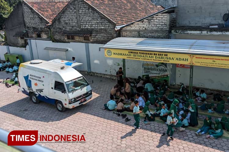 Para siswa saat membaca buku yang dibawa mobil pintar atau perpustakaan keliling (Foto: Akmal/TIMES Indonesia).