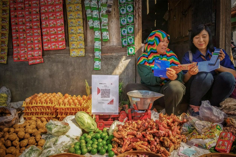 Petugas BRI membantu pedagang sayur untuk memproses transaksi keuangan. (foto: dok BRI)
