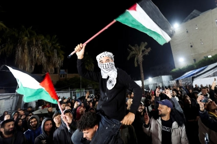 Orang-orang mengibarkan bendera Palestina di Deir el-Balah (FOTO B: Al Jazeera/Reuters)