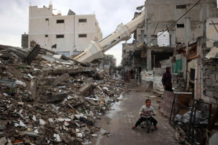 Seorang anak Palestina mengendarai sepeda di dekat menara masjid yang runtuh selama bulan puasa Ramadan di kamp pengungsi Nuseirat di Jalur Gaza tengah pada 7 Maret 2025. (FOTO: AFP)