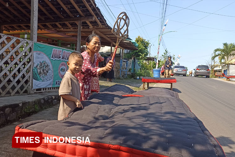Salah satu warga Desa Kemiren bersama cucunya sedang memukul kasur dengan rotan. (FOTO: Ikromil Aufa/TIMES Indonesia)