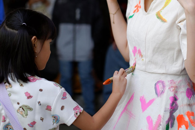 Bocah perempuan menyapukan kuas ke gaun yang dipakai oleh model dalam acara Freestyle Art Gown, kolaborasi Tim ERIOS Mahasiswa Ilmu Komunikasi Universitas Muhammadiyah Malang bersama AION Studio di kawasan Kayutangan Heritage. (Foto: dok TIM ERIOS)