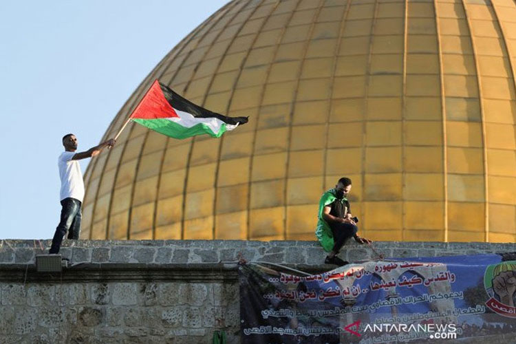 Seorang pemuda Palestina mengibarkan bendera dengan latar belakang Dome of the Rock. Inggris, Kanada, dan Prancis serta negara-negara Eropa berencana mengakui Palestina sebagai negara berdaulat. (foto: Reuters/Antara)