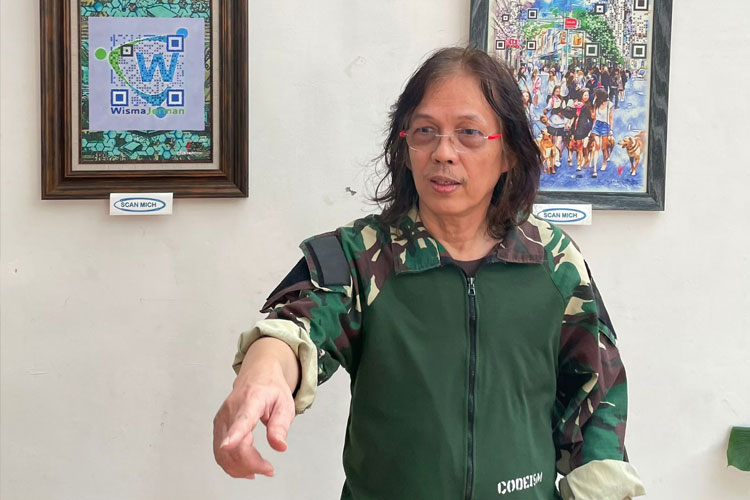 Doddy 'Mr D' Hernanto berlatar QR Art codeisme karyanya yang tampil di Wisma Jerman Surabaya, Sabtu (23/8/2025). (FOTO: Dok.Pribadi)