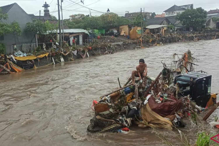 Seorang warga duduk di atas sebuah ekskavator yang hanyut terbawa banjir di Tukad Badung, Denpasar Barat, Bali, Rabu (10/9/2025). (ANTARA/Rolandus Nampu)