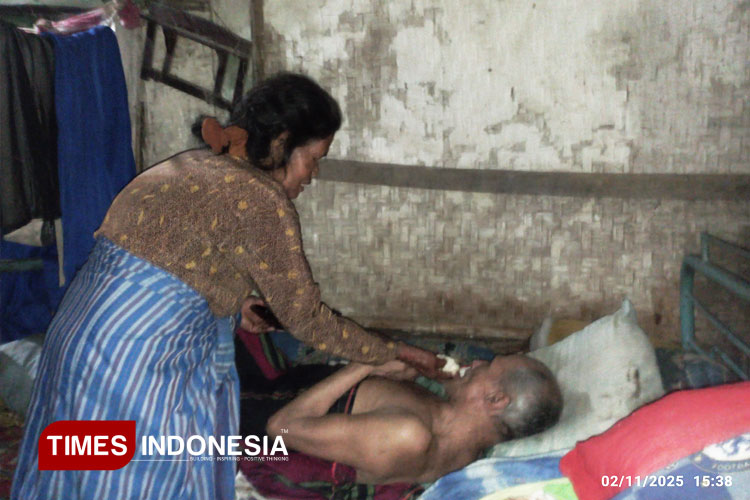 Bik Ni (65), warga Desa Brongkal Pagelaran Kabupaten Malang, saat merawat suaminya yang sakit menahun, di rumah mereka yang  kumuh dan tak layak huni, Minggu (2/11/2025) petang. (FOTO: Amin/TIMES Indonesia)